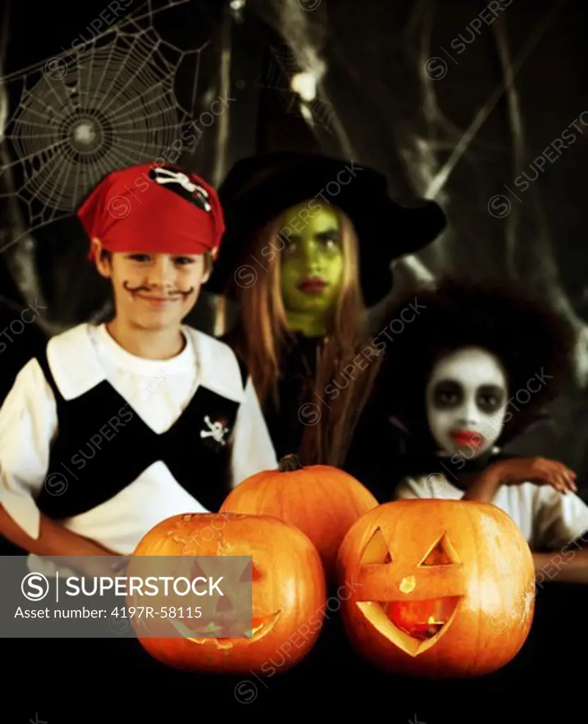 Portrait of three children dressed up for Halloween with jack-o-lanterns in front of them