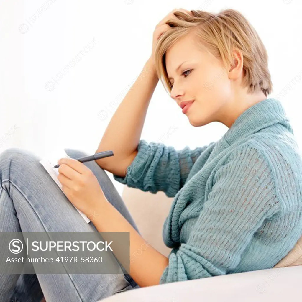 An attractive young female writing in her diary on the couch