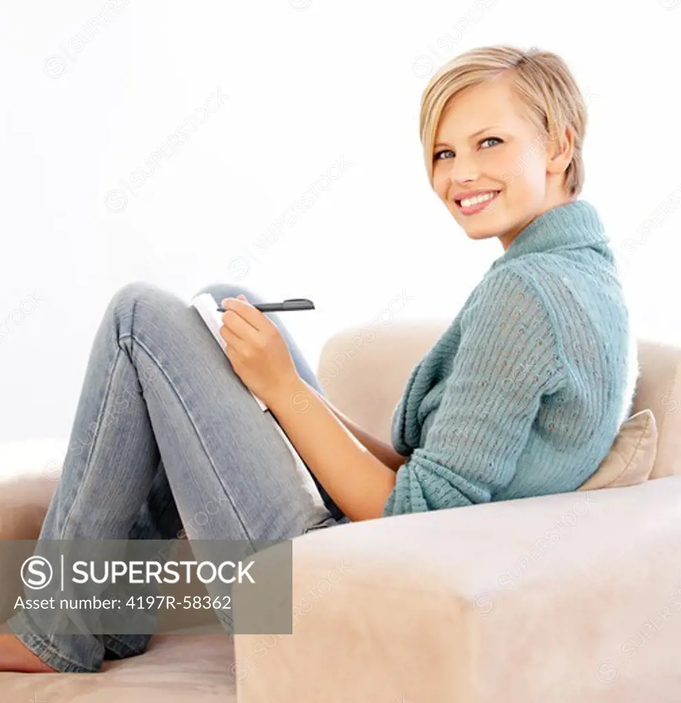 An attractive young female smiling and writing in her diary on the couch