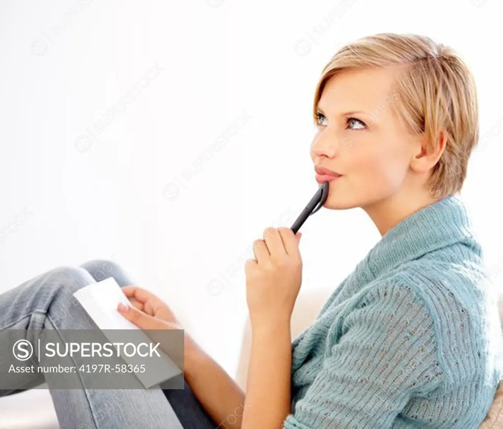 An attractive young female thinking and writing in her diary on the couch