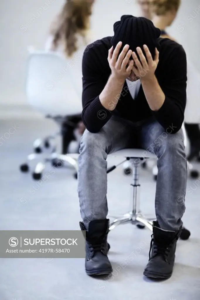 A young man holds his head in his hands while taking a moment for himself in a therapy session