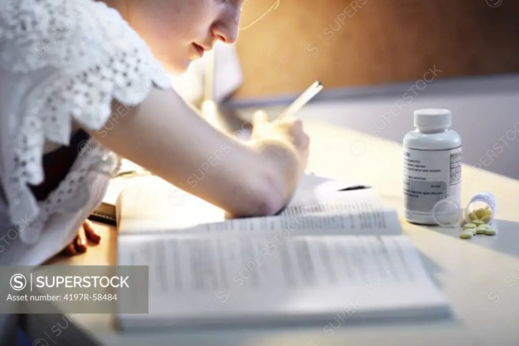 A young woman using medication to help stay awake to study deep into the night