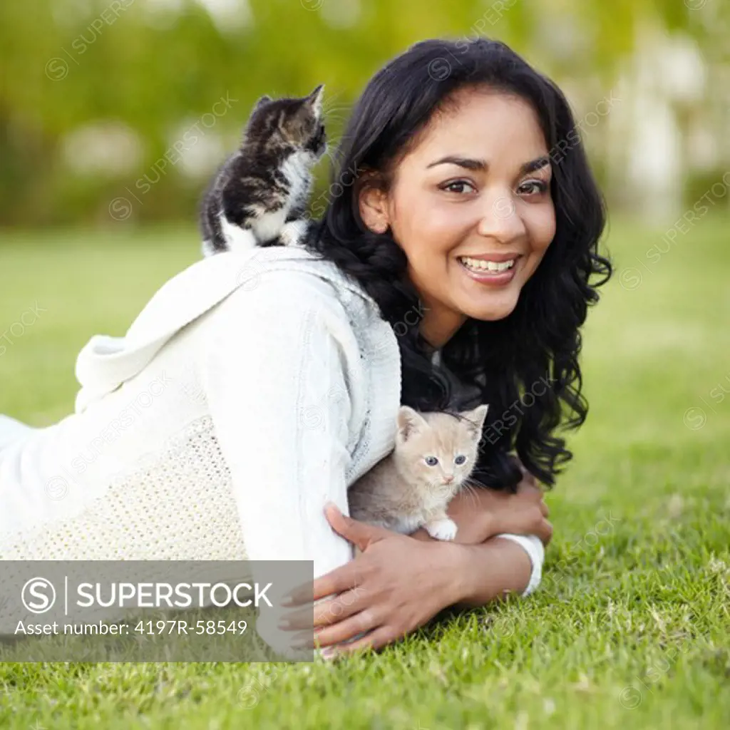 Pretty young woman lying on the grass outdoors with her kittens