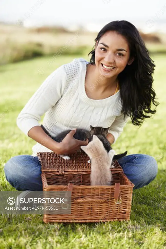 Cute young woman putting her little kittens in a wicker basket on the grass outdoors