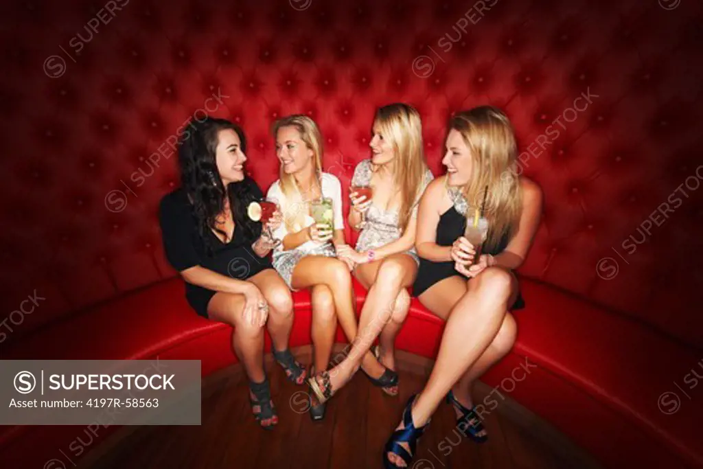 Four beautiful girls enjoying cocktails in a booth at an elite club
