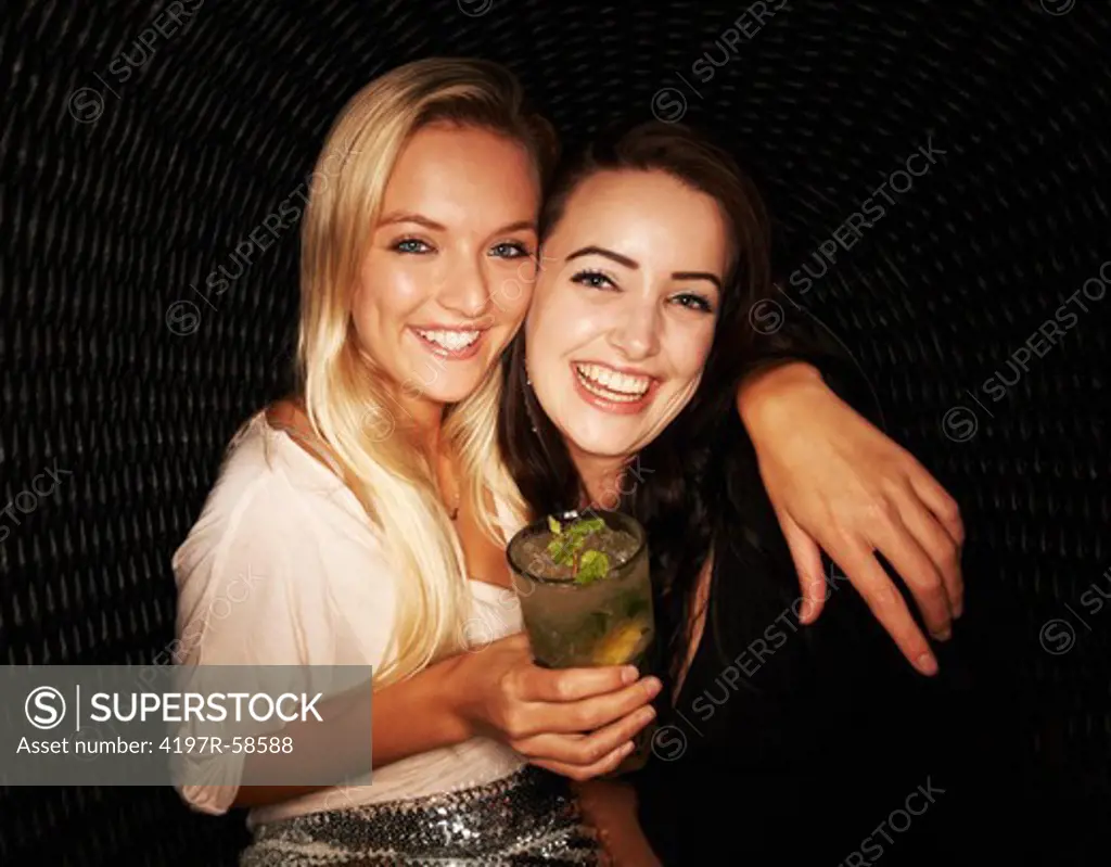 Portrait of two pretty young girls drinking cocktails while out partying