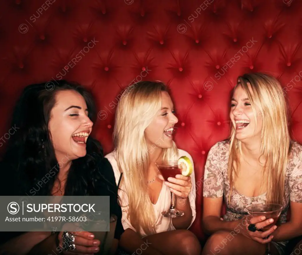Three pretty young girls laughing together while enjoying cocktails on a night out