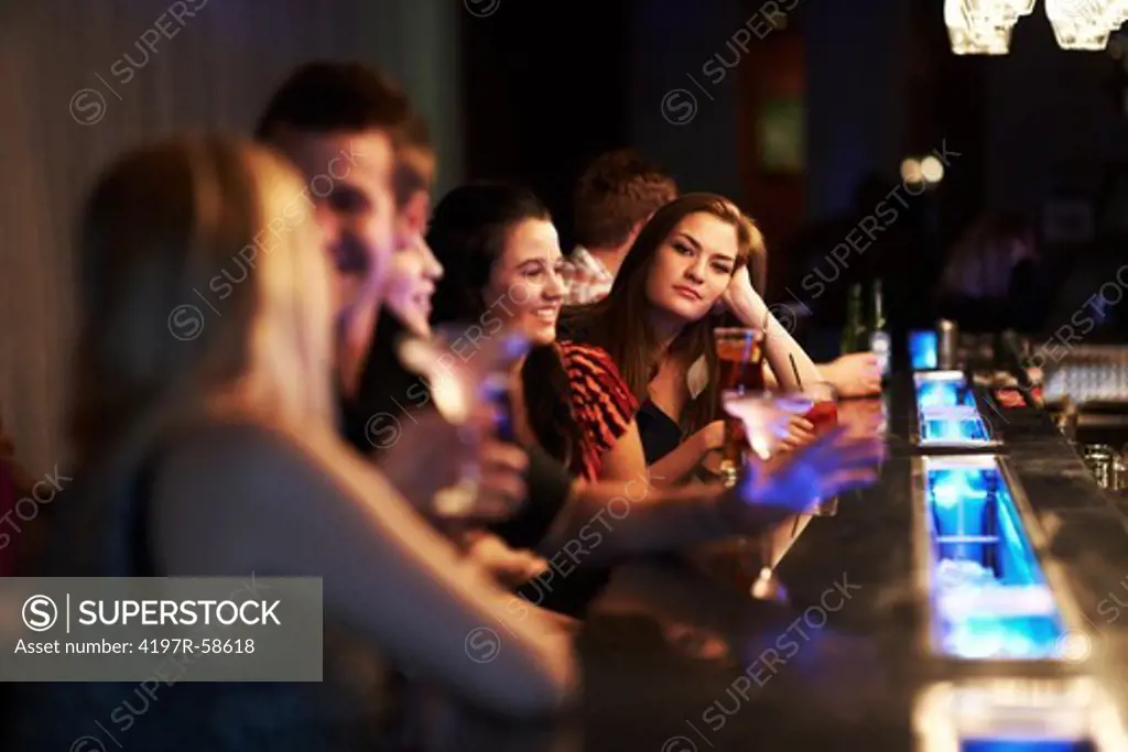Portrait of a pretty young woman leaning on her hand at the bar while others converse