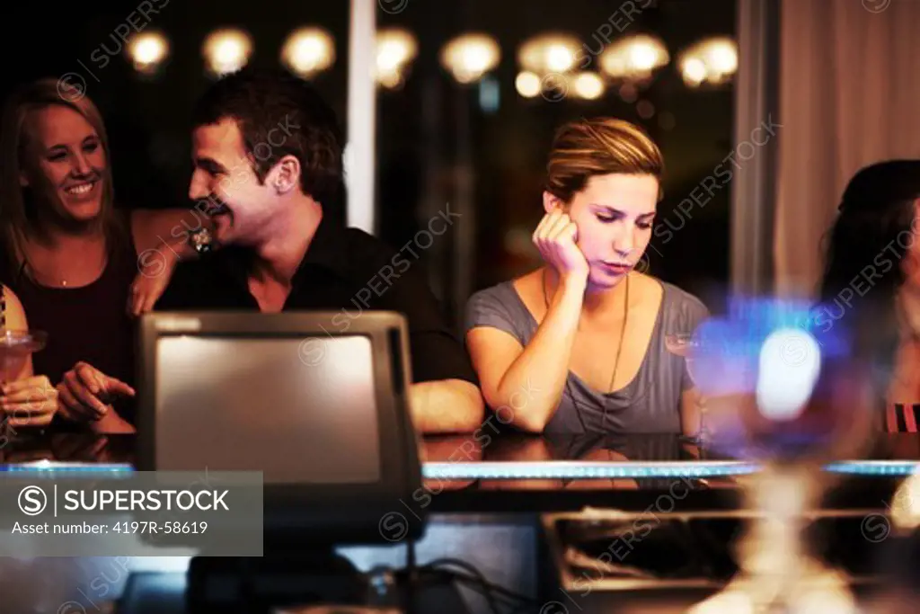 A pretty young woman checking her phone while standing at the bar