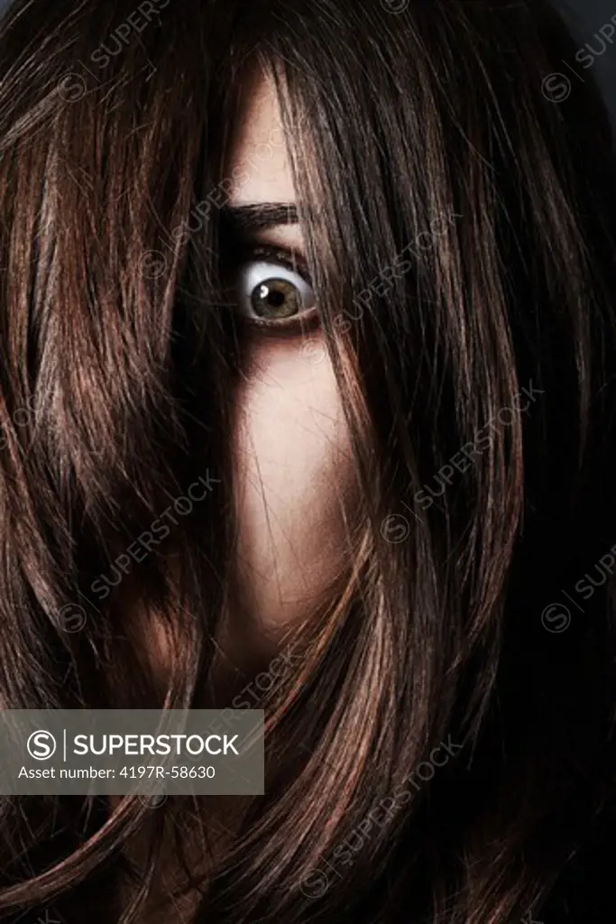 A studio concept shot of a mentally disturbed young woman with only one eye showing through hair draped over her face