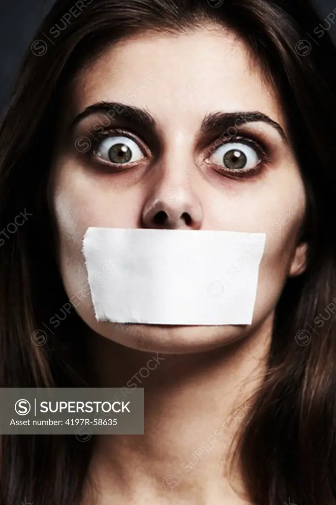 A studio concept shot of a disturbed young woman with her mouth taped shut