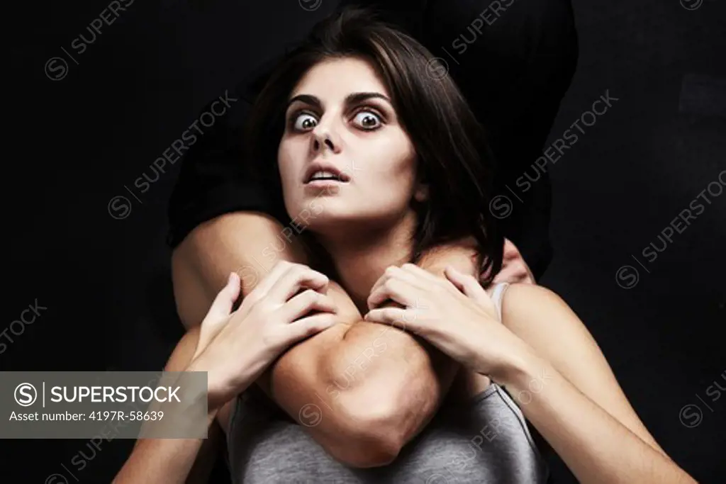 A studio concept shot of a mentally disturbed young woman being choked from behind by a masculine arm