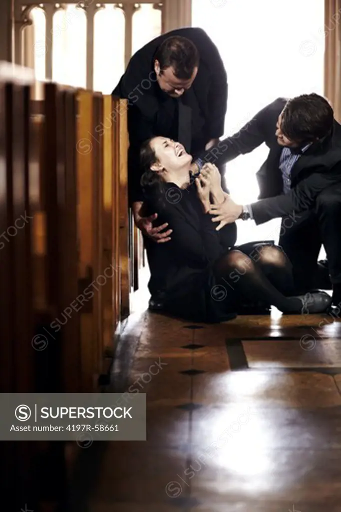 A young woman being helped up after she has fallen to the floor grief-stricken at a funeral
