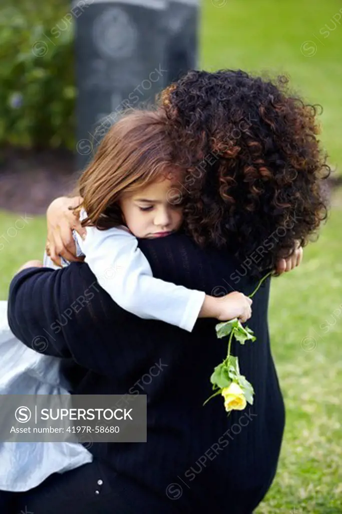 A young mother embracing her little girl at the grave of a family member