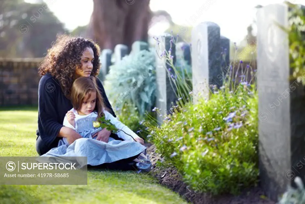 A little girl sitting on her mother's lap while they visit a deceased family member's grave