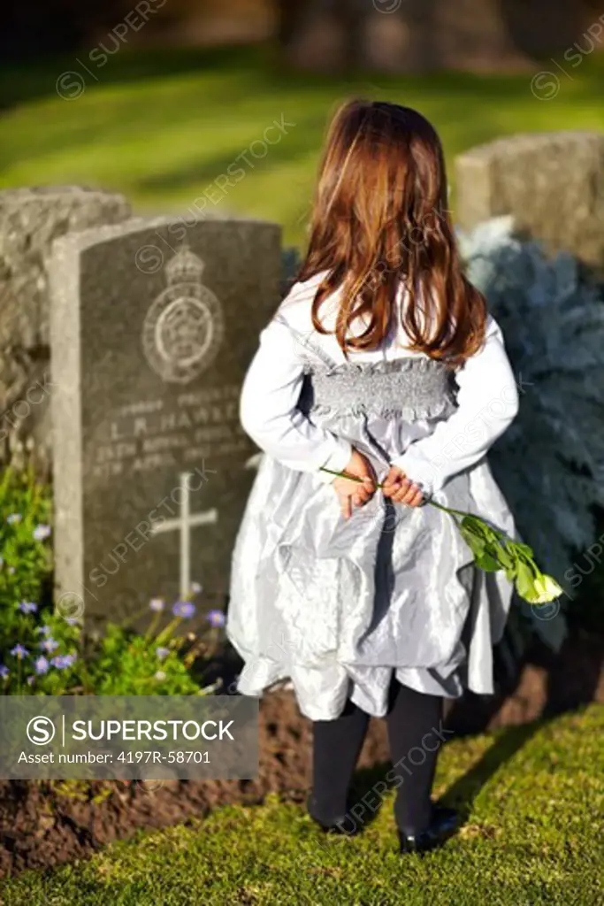 Rearview of a little girl standing at a gravestone while holding a yellow rose