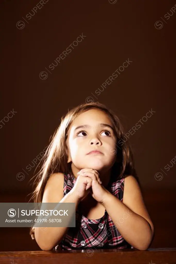 A cute little girl with her hands together praying in church
