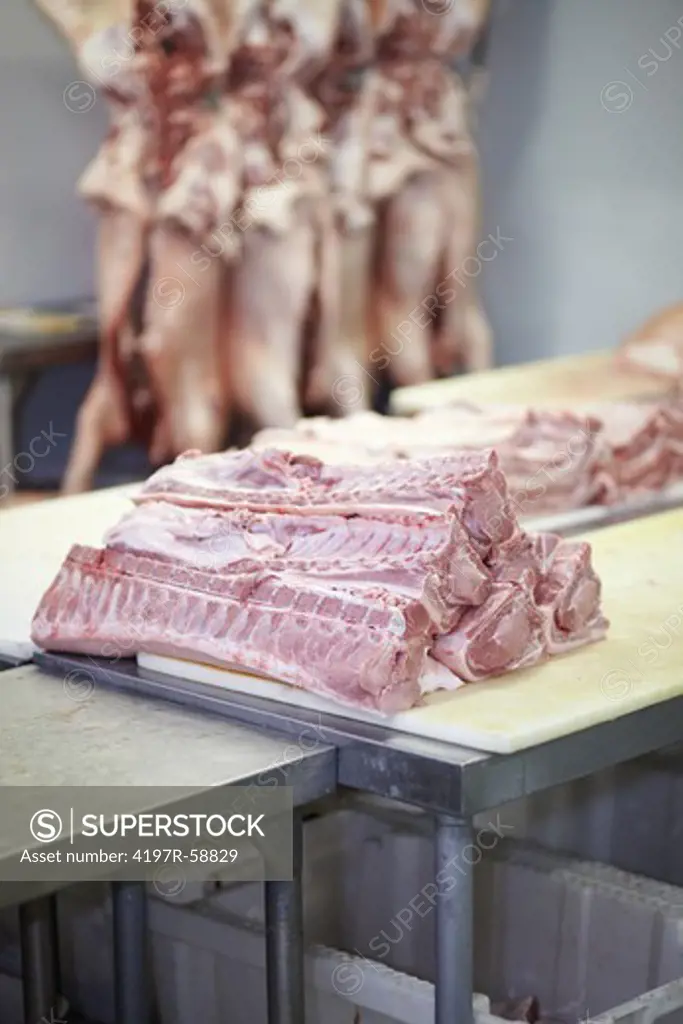 Selection of meat cuts on a counter with carcasses hanging in the background