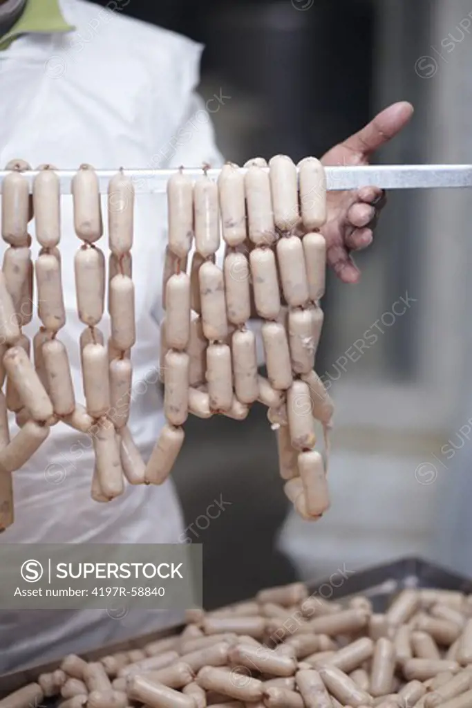 Butcher holding up a rack of raw sausages - cropped