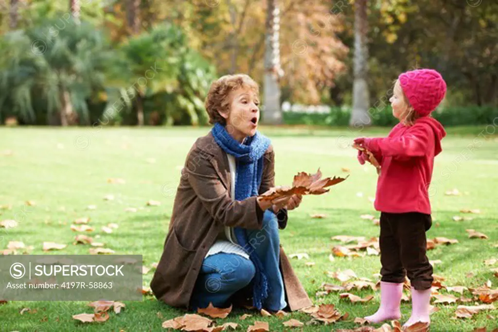 A grandmother and her granddaughter playing outside with leaves