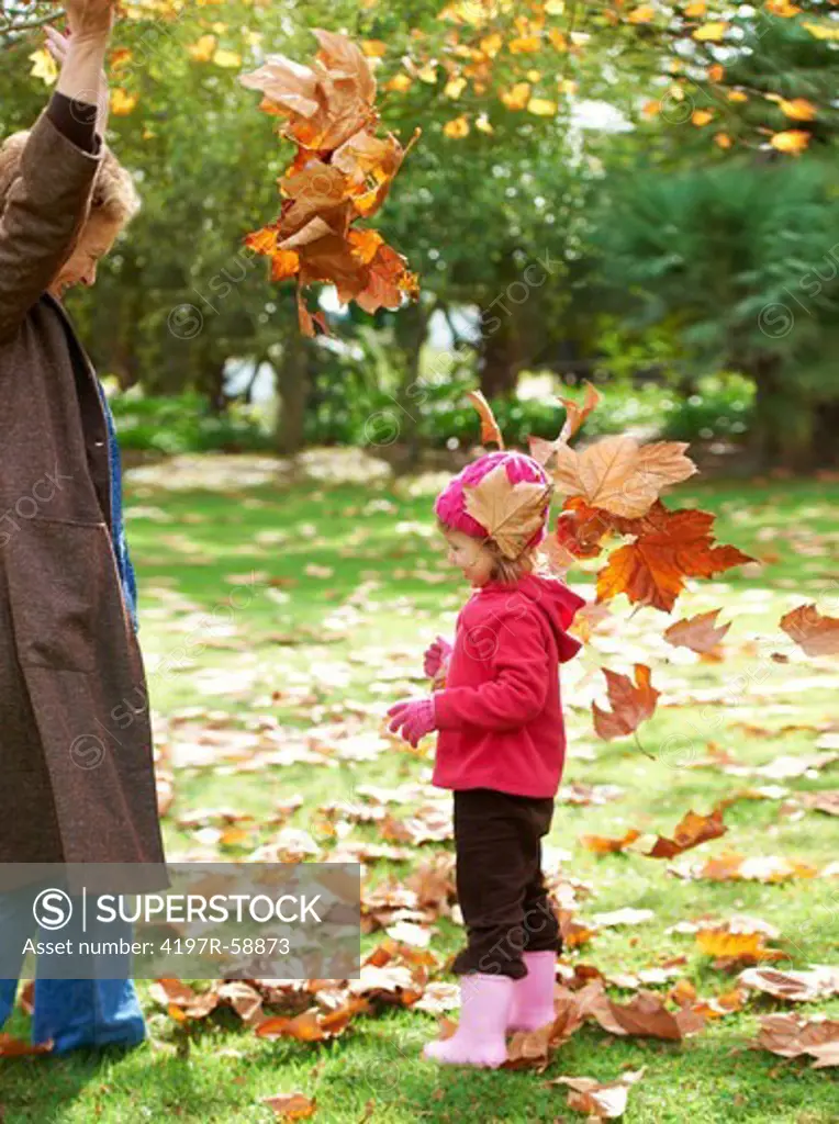 A grandmother throwing leaves outside with her granddaughter