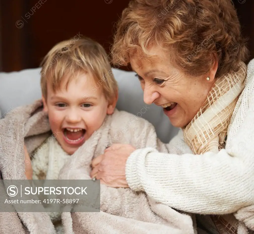 A grandmother tickling her grandson while sitting on the couch
