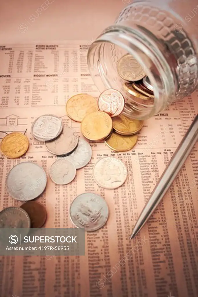 Shot of a tipped over maney jar with its contents spilling over the financial section of a newspaper
