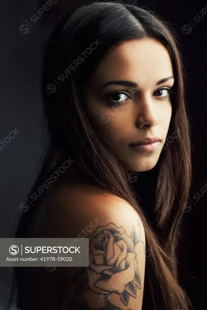 Gorgoeous young hispanic woman gazing at you over her tattooed shoulder