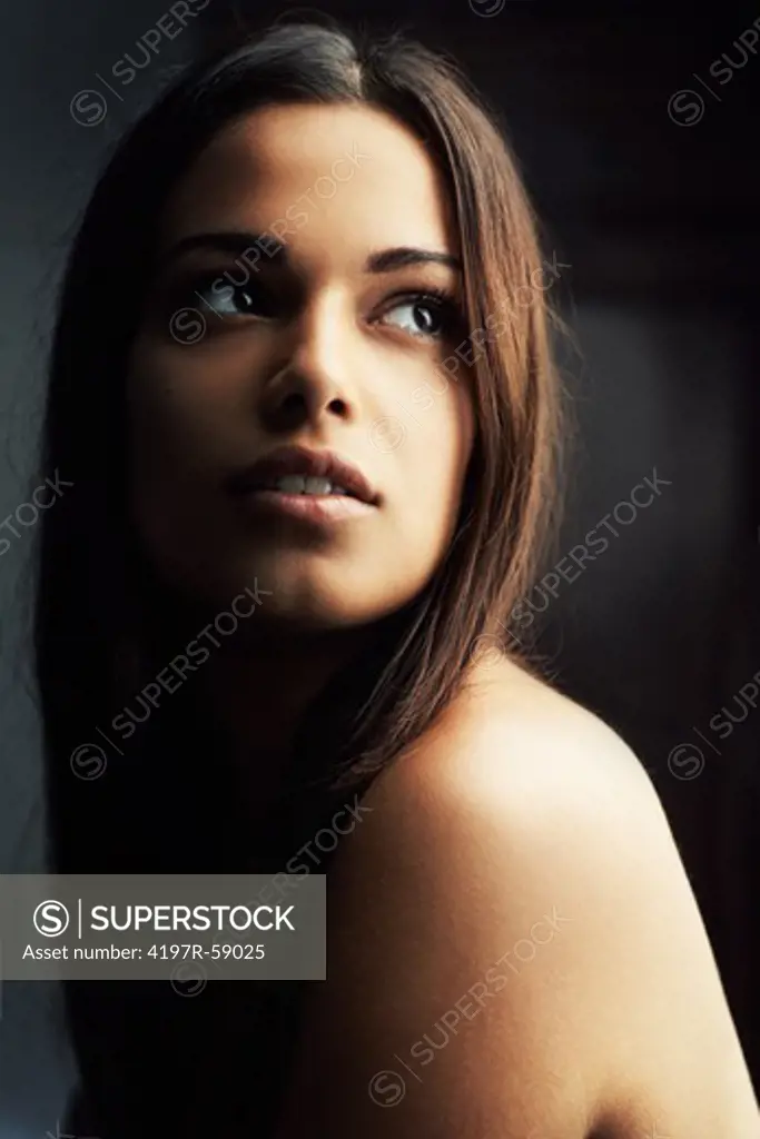 Stunning young woman with soft smooth skin gazing upwards with shadowy background