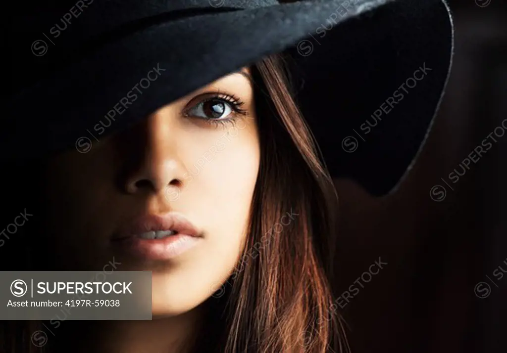 Beautiful hispanic woman's face framed by her hair and hat in deep shadows