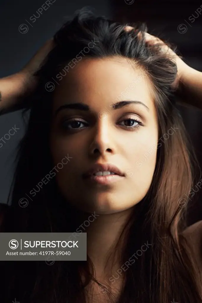Close up of a sultry hispanic woman gazing at you with her hands in her hair