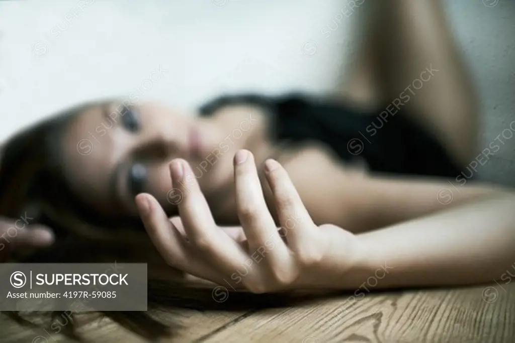 Image of a woman lying on the ground, focus on her limp hand in the foreground