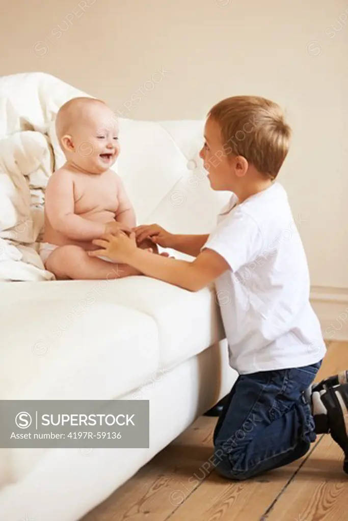 A young boy and his baby sister laughing while sitting on the couch