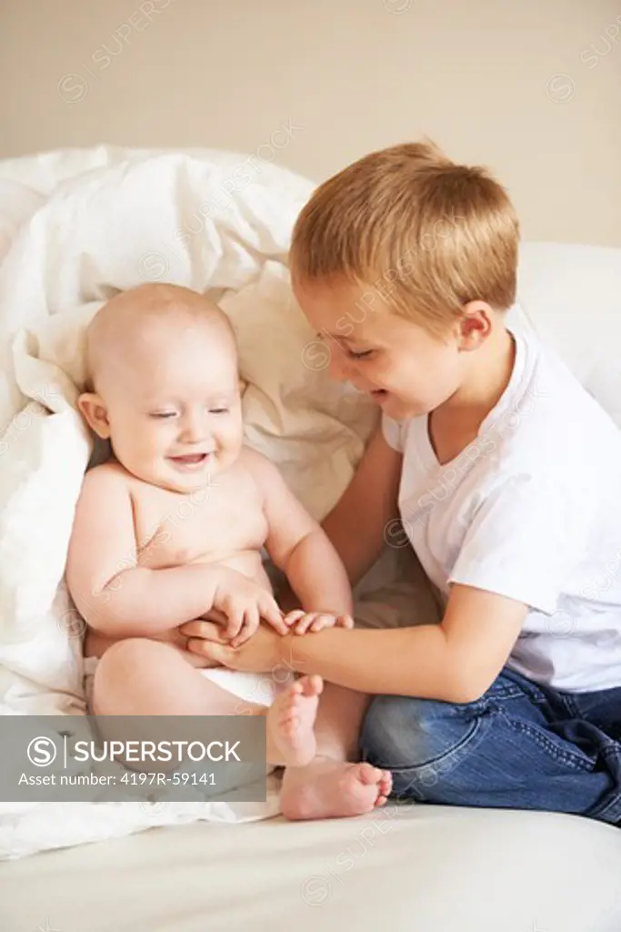 A playful young boy and his baby sister sitting on the couch