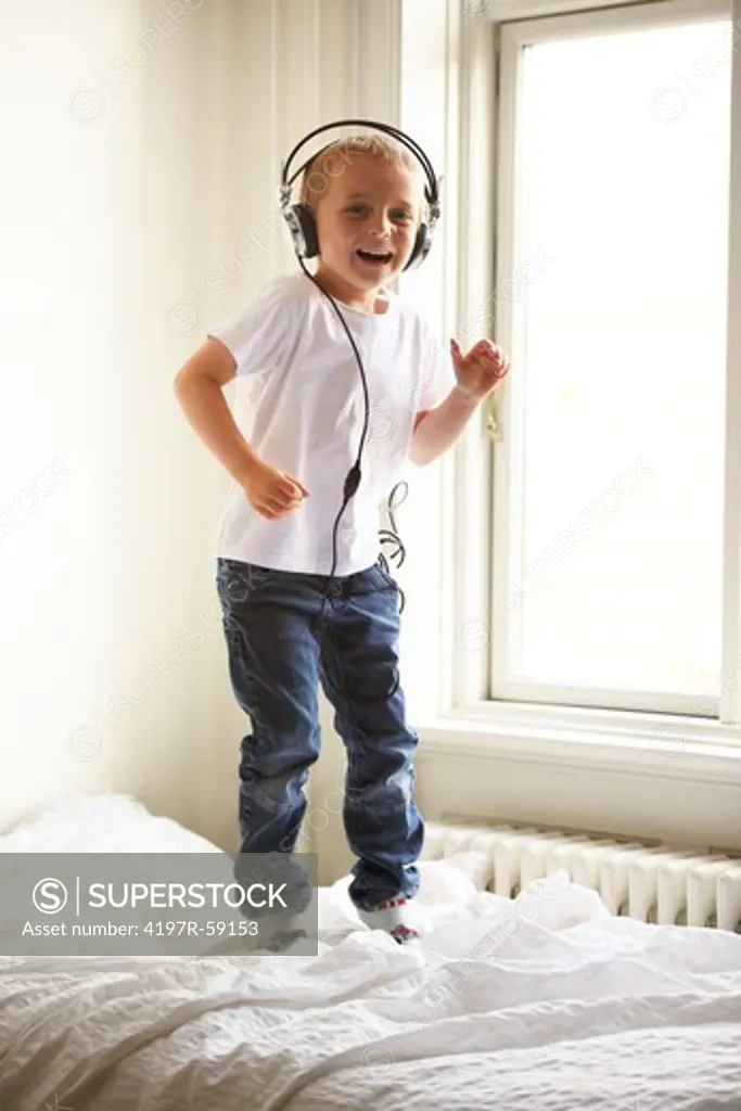 Portrait of a young boy listening to music and jumping on his bed