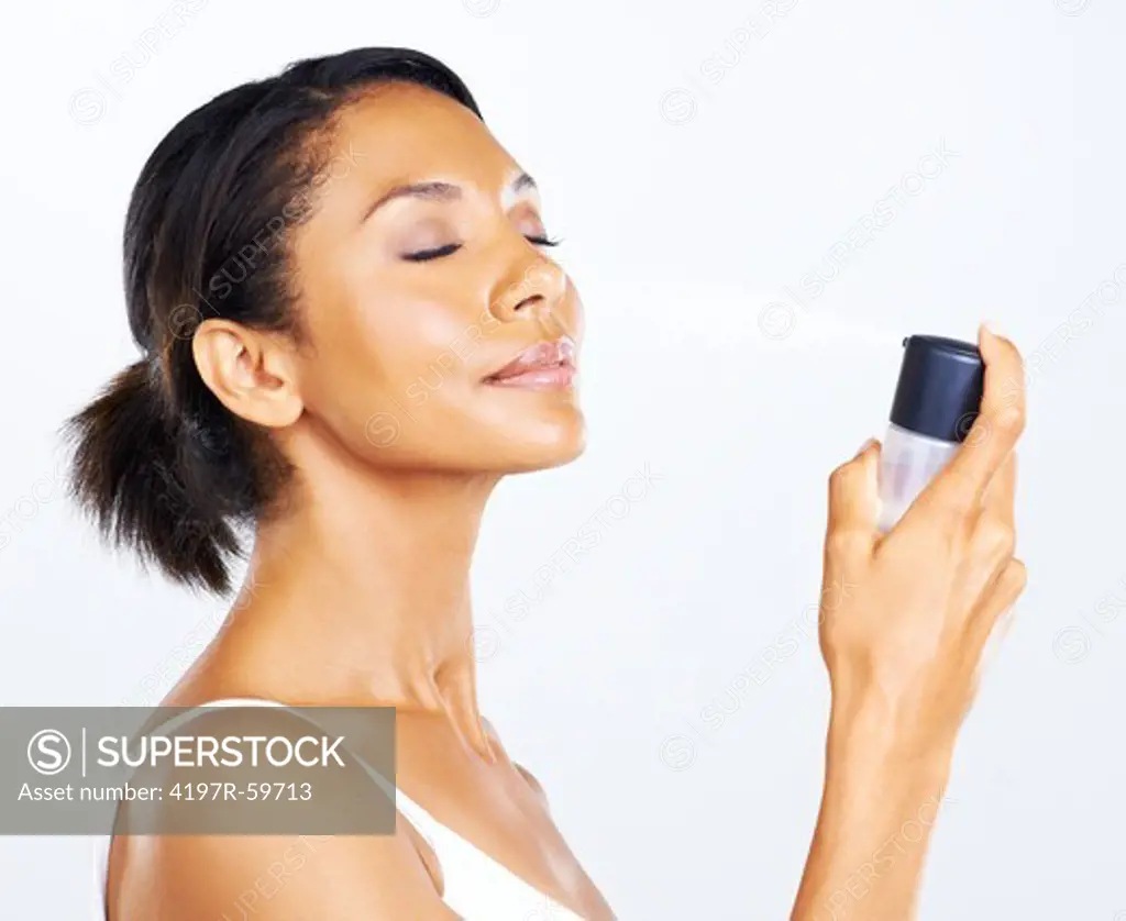 A pretty young woman spraying water onto her face to rehydrate her skin