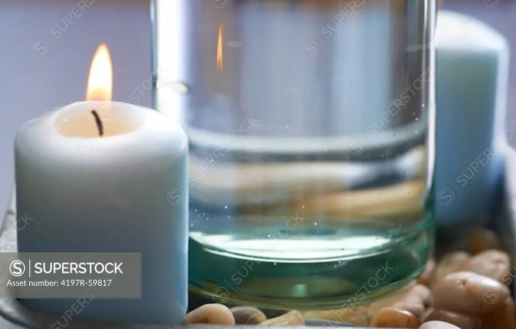 Closeup of a lit aromatic candle alongside a clear, still glass bottle of water