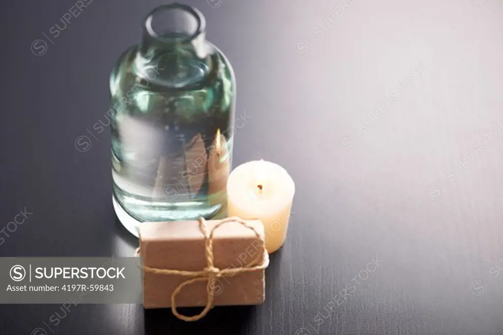 A calming spa arrangement consisting of a cake of soap, a lit aromatic candle and a clear jug of water - Copyspace