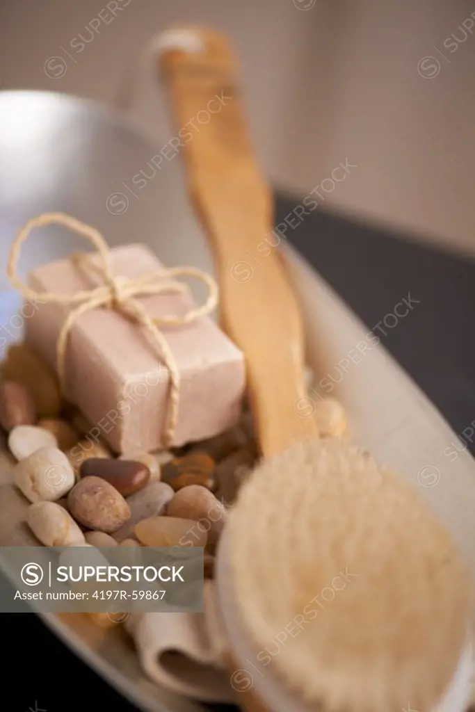 An exfoliating brush, smooth pebbles and a cake of soap inside of a shallow silver tray
