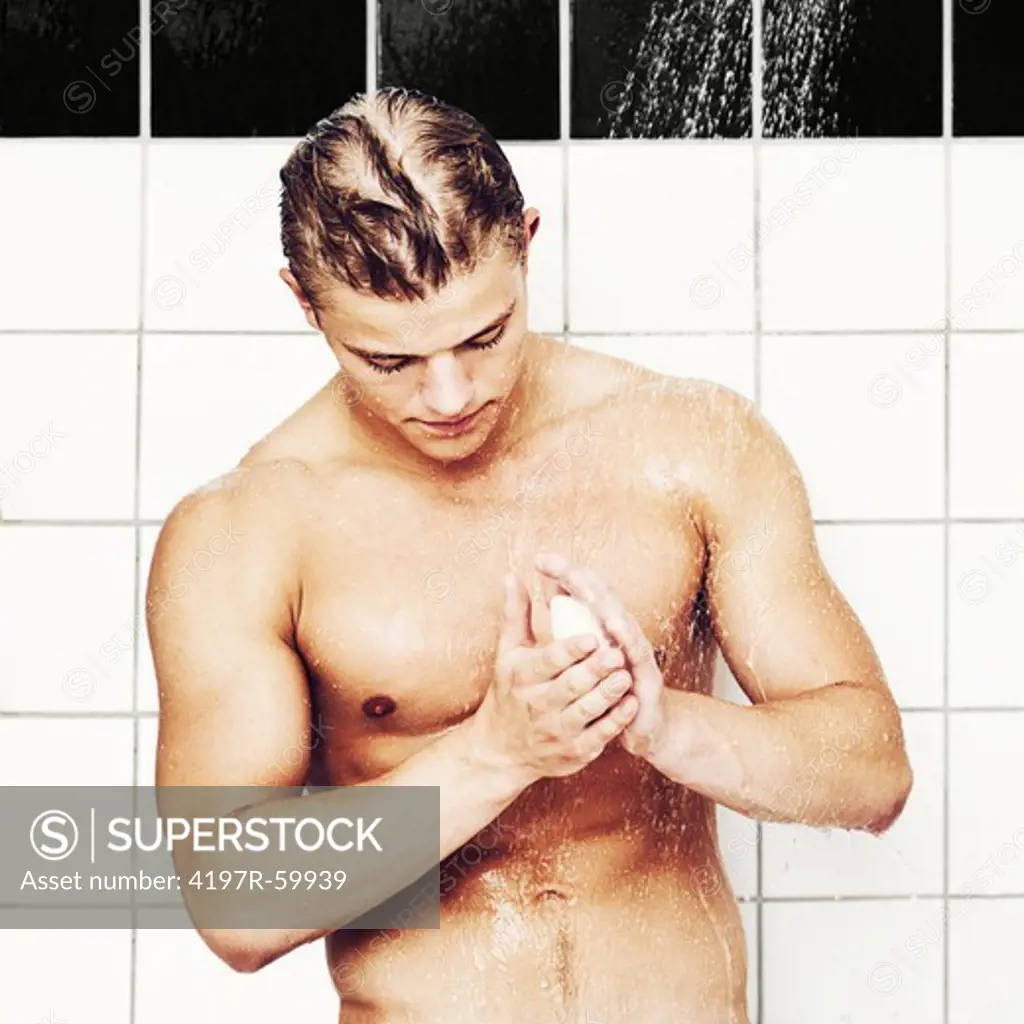 A hunky young man holding the soap in the shower
