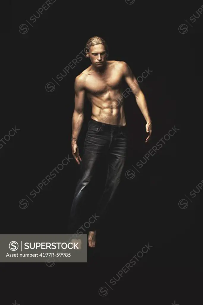 A handsome young man wearing only jeans floating on a black background