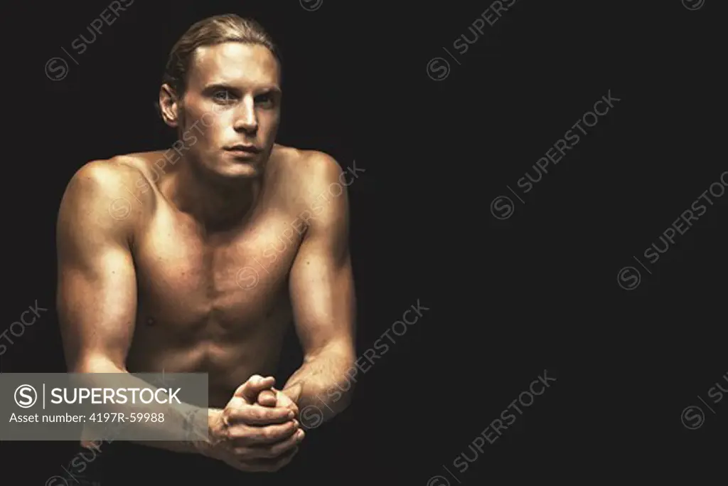 Portrait of a handsome young man wearing only jeans and sitting on a black background