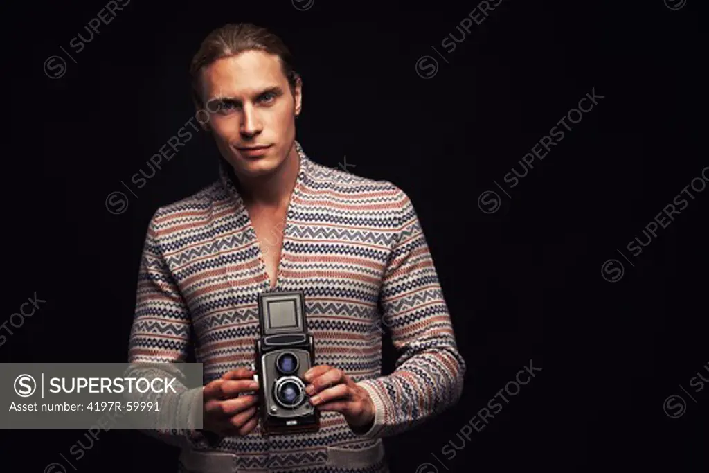 Portrait of a handsome young man holding a vintage twin lens reflex camera on a black background