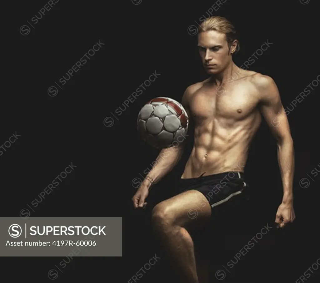 A handsome young shirtless man bouncing a soccer ball on his knee
