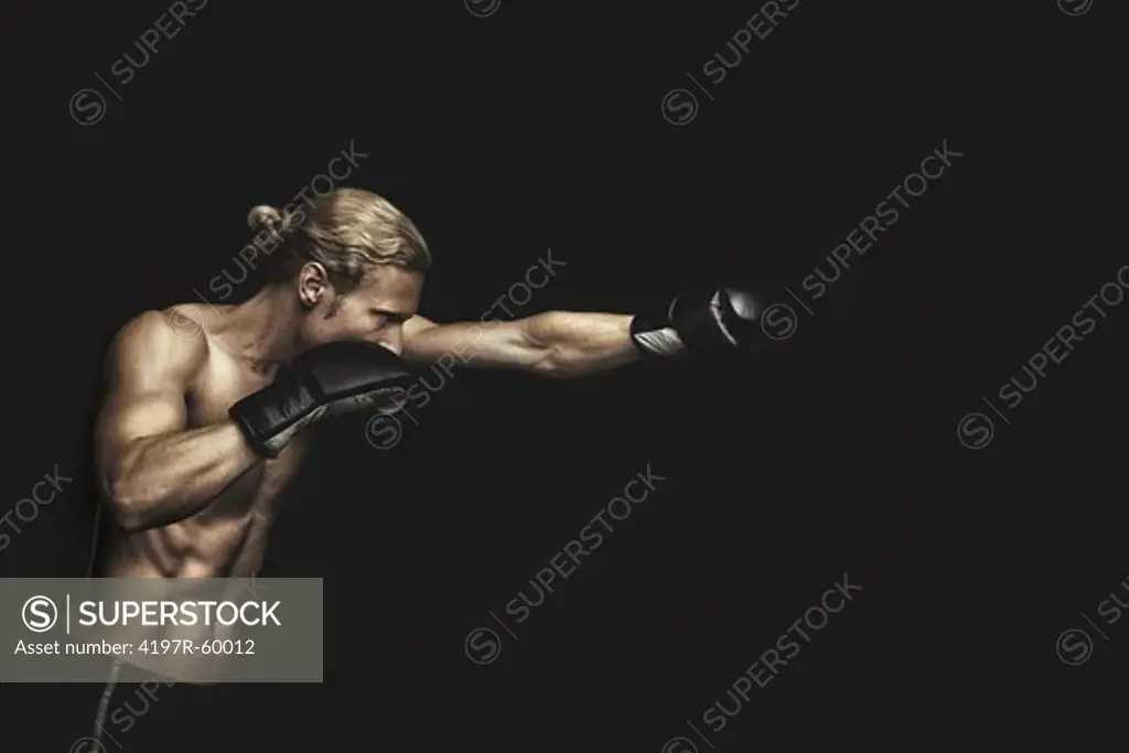 Profile of a young man punching while wearing boxing gloves on a black background
