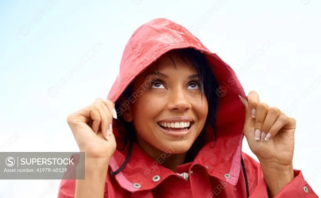 Young woman smiling and holding on to the hood of her red raincoat