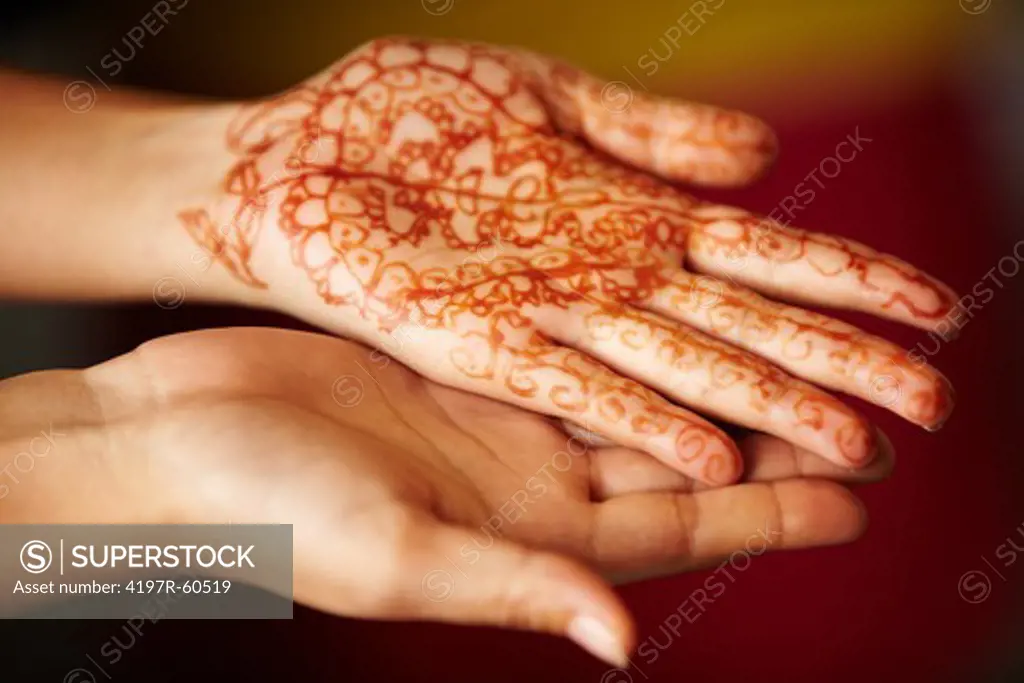 Two female hands with traditional henna painted on one palm