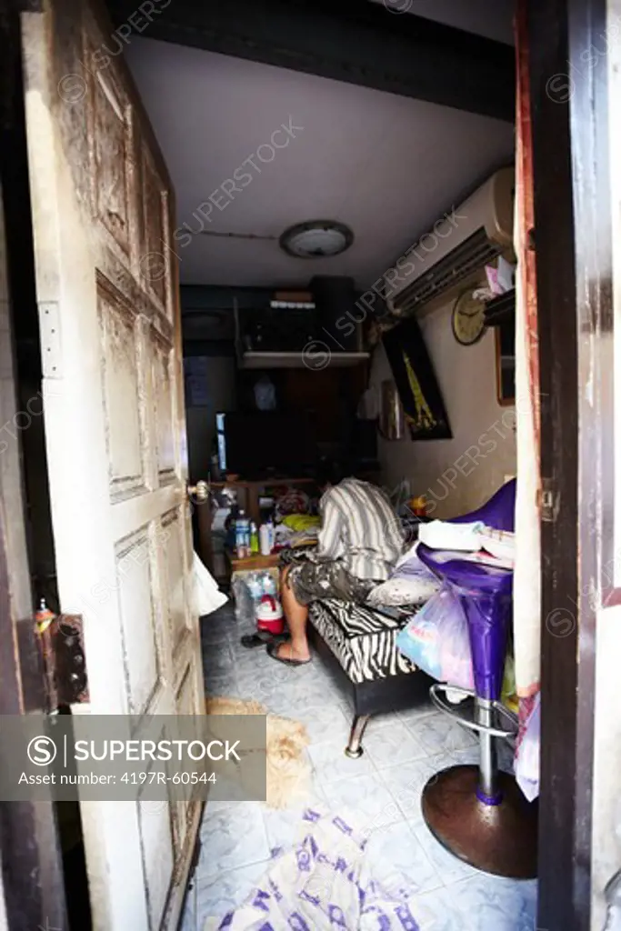 Rearview of a Thai man siiting on his bed on his small and messy room