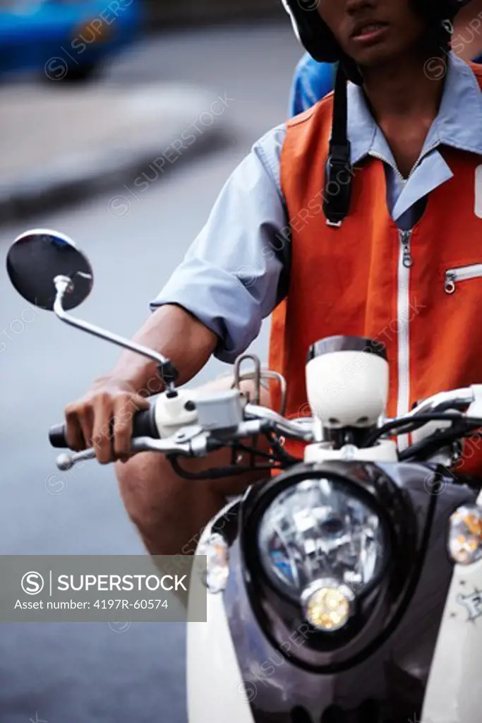 Cropped view of a young Asian man riding a scooter in the street