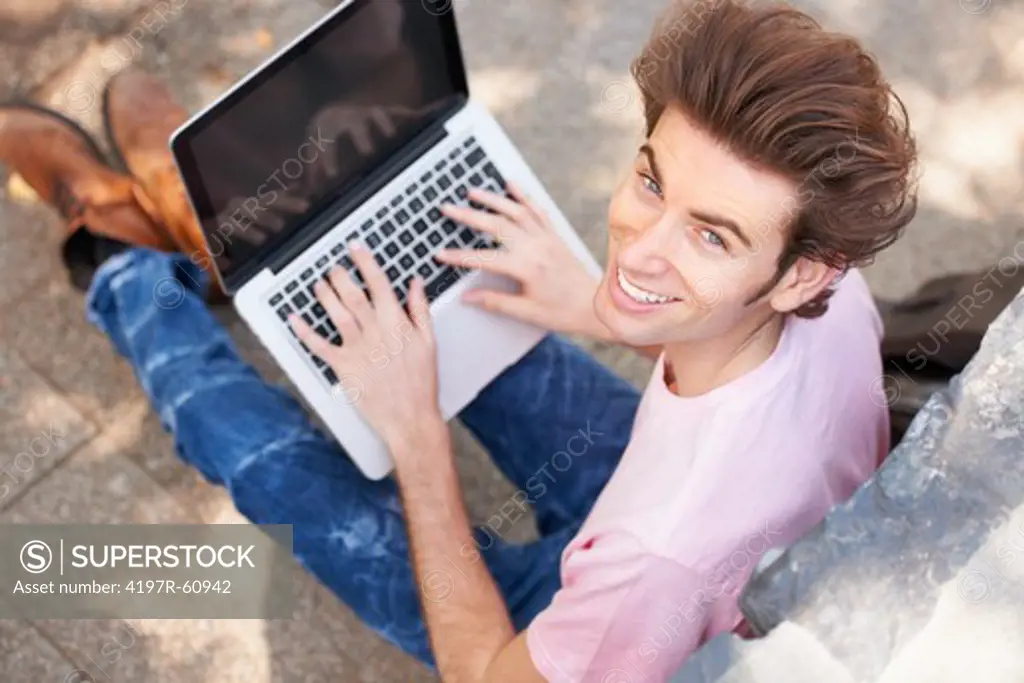 An upwards shot of a happy trendy male on his laptop sitting outside